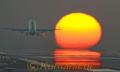 滑走路の延長線上に沈む夕日に向かって飛び立つ旅客機。エンジンの排気が太陽